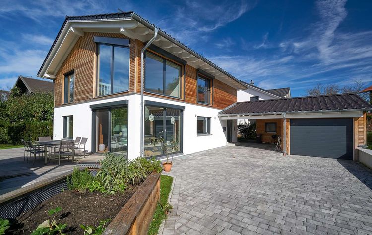 Modernes Holzhaus im Landhausstil mit Mischfassade aus Holz und mineralischem Außenputz und vielen Glaselementen
