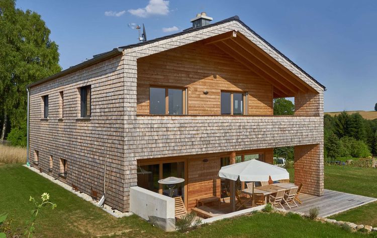 Modernes Holzhaus mit Holzverschindelung aus Tannenholz und geschützem Balkon- und Terrassenbereich
