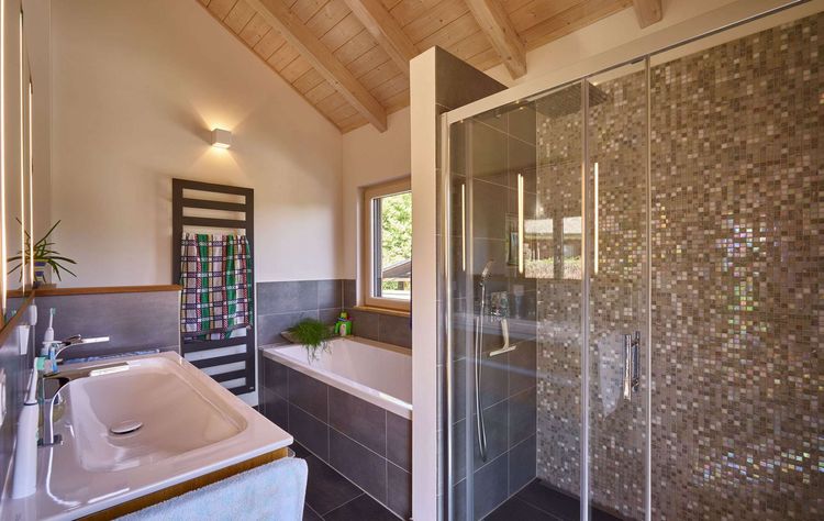 Das Badezimmer des modernen Holzhauses im Landhausstil mit Holzfassade aus Lärchenholzbohlen und Doppelcarport