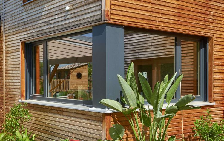Das Eckfenster des modernen Holzhauses im Landhausstil mit Holzfassade aus Lärchenholzbohlen und Doppelcarport