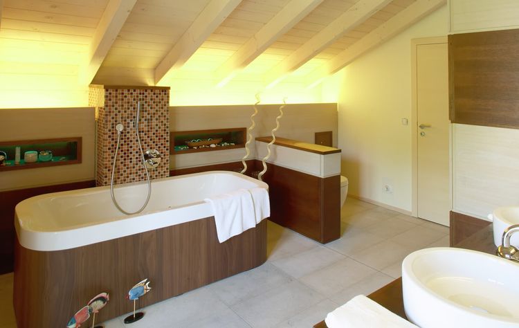 Das Badezimmer des Holzhauses im Landhausstil mit geschickt eingesetzte Mischfassade aus mineralischem Außenputz und Lärchenholz und Schiebläden, die elektrisch verstellbar sind