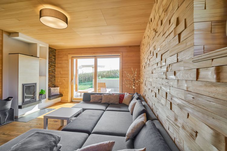 Das gemütliche, komplett mit Holz verkleidete Wohnzimmer des modernen Holzhauses mit Holzverschindelung aus Tannenholz und geschützem Balkon- und Terrassenbereich
