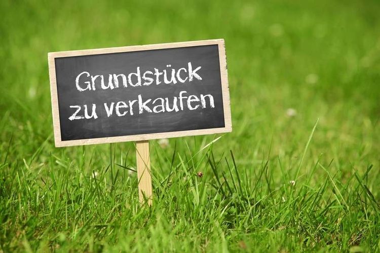 Grüner Rasen mit "Grundstück zu verkaufen"-Schild