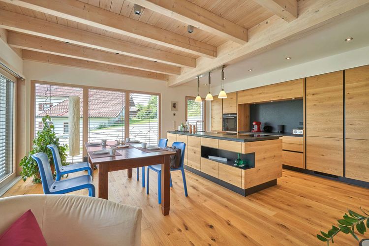 Die Küche des modernen Holzhauses mit Pultdach und Mischfassade aus mineralischem Außenputz und Lärchenholz, ein Knick im Grundriss sorgt für den perfekten Ausblick