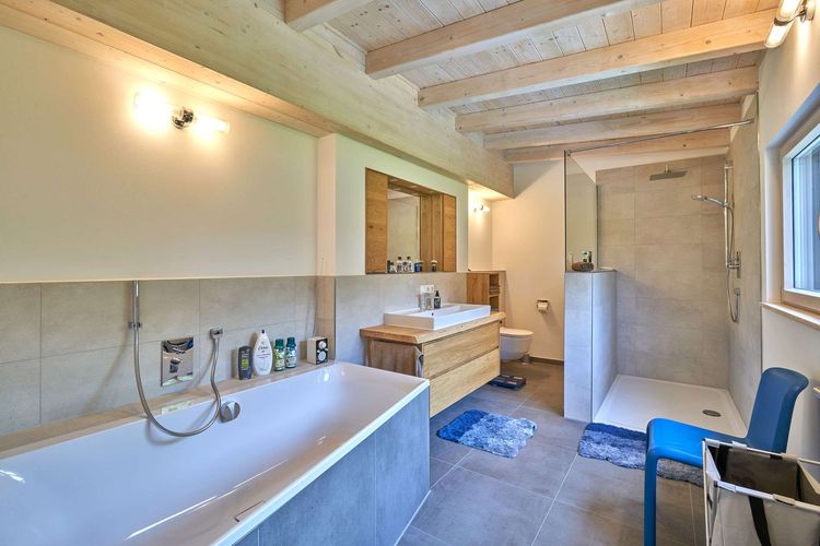 Das Badezimmer des modernen Holzhauses mit Pultdach und Mischfassade aus mineralischem Außenputz und Lärchenholz, ein Knick im Grundriss sorgt für den perfekten Ausblick