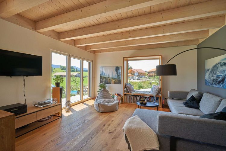 Das Wohnzimmer des modernen Holzhauses im Landhausstil mit durchgängiger Lärchenholzfassade und Holz-Alu-Fenstern
