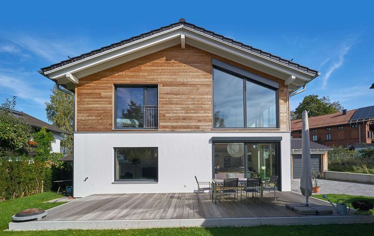 Modernes Holzhaus im Landhausstil mit Mischfassade aus Holz und mineralischem Außenputz und vielen Glaselementen