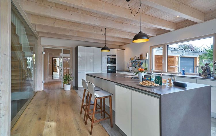 Die Küche des modernen Holzhauses im Landhausstil mit Mischfassade aus Holz und mineralischem Außenputz und vielen Glaselementen