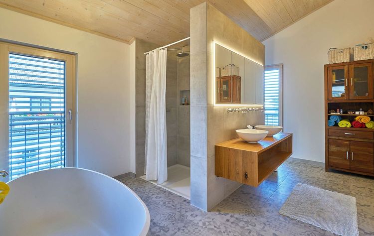 Das Badezimmer des modernen Holzhauses im Landhausstil mit Mischfassade aus Holz und mineralischem Außenputz und vielen Glaselementen