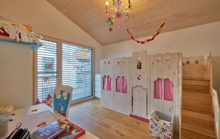 Das Kinderzimmer des modernen Holzhauses im Landhausstil mit Mischfassade aus Holz und mineralischem Außenputz und vielen Glaselementen