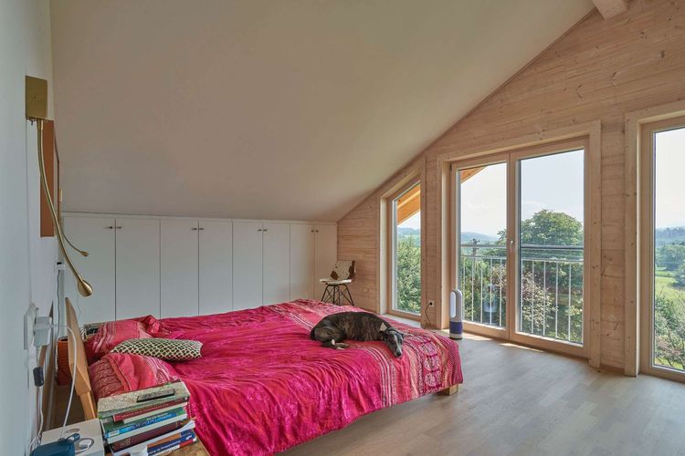 Das Schlafzimmer des modernen Holzhauses im Landhausstil mit Holzfassade, Holz-Alu-Fenstern und großzügigen Balkonen