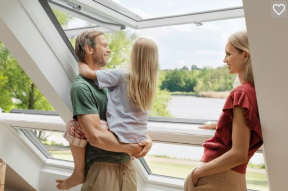 Familie steht im Dachgeschoss an einem VELUX-Dachfenster und schaut ins Grüne