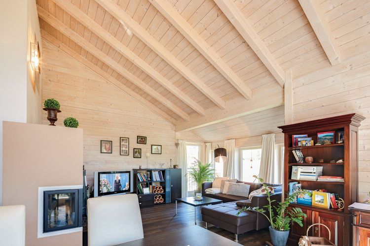 Das Wohnzimmer mit Kachelofen des Bungalows aus Holz auf Hanggrundstück mit ausgebautem Keller mit viel Glas