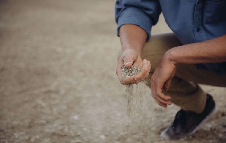 Mann in der Hocke lässt Sand aus seiner Hand rieseln