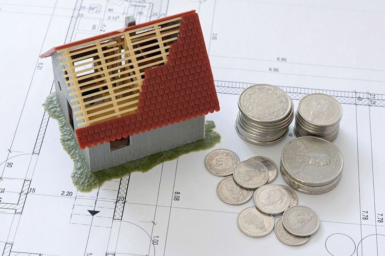 Kleines Modellhaus auf einem Grundriss mit einigen Geldmünzen