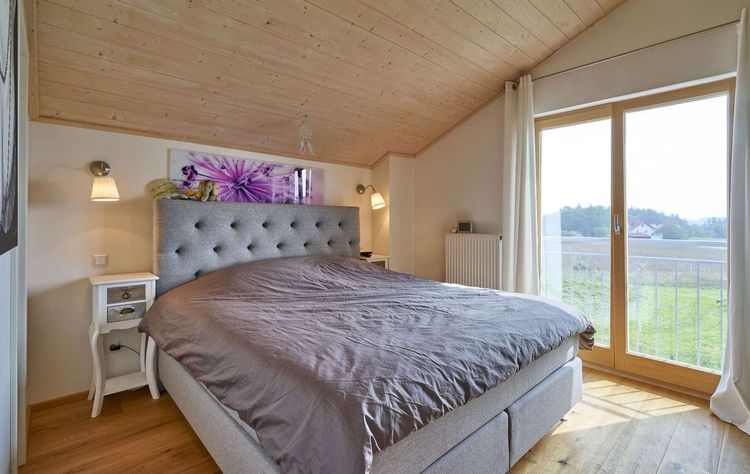 Das Schlafzimmer des traditionellen Holzhauses mit Mischfassade aus Lärchenholz und Putz, mit flachem Satteldach und hohem Kniestock