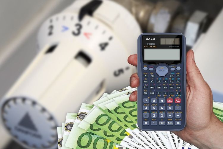 Eine Person hält einen Taschenrechner mit Geldscheinen und Heizkörper im Hintergrund