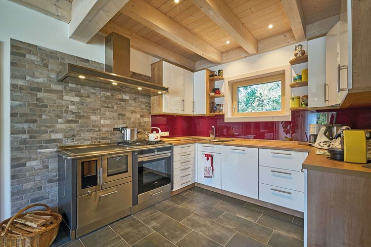 Die Küche des modernen Holzhauses im Landhausstil mit flachem Satteldach und gemischter Fassade aus Lärchenholz und mineralischem Außenputz