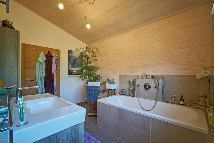 Das Badezimmer des modernen Holzhauses im Landhausstil mit flachem Satteldach und gemischter Fassade aus Lärchenholz und mineralischem Außenputz