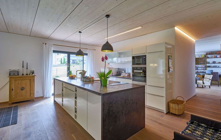 Die Küche des modernen Holzhauses im Bauhausstil mit drei Gebäudetrakten, zwei davon mit mineralischem Außenputz und Flachdach, einer mit Holzfassade aus Fichtenholzbohlen und Pultdach
