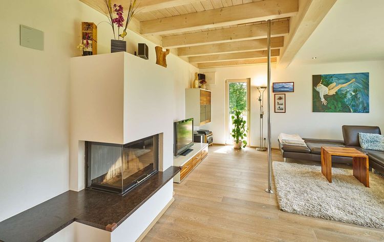 Der Kachelofen des modernen Holzhauses im Landhausstil mit Mischfassade aus Fichtenholz und mineralischem Außenputz