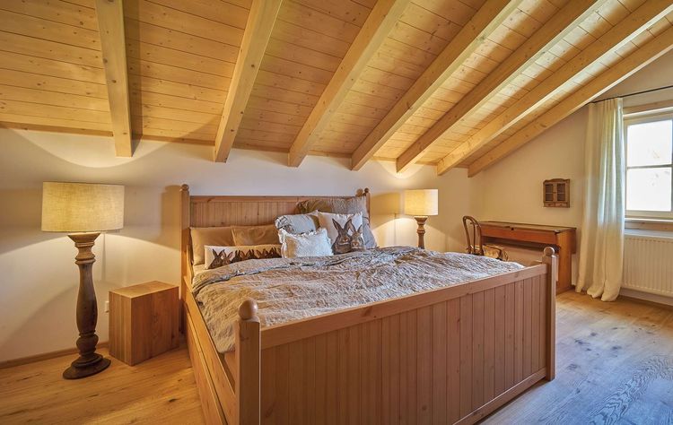 Das Schlafzimmer des traditionellen Holzhauses mit durchgängiger Holzfassade, innen viel sichtbarem Holz und moderner Haustechnik