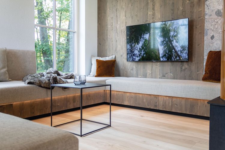 Das Wohnzimmer mit umlaufender Couch des modernen und großzügigen Holzhauses, bzw. Massivholzhauses im Landhausstil im Musterhauspark in Ortenburg. Der Neubau erinnert an die Chalets im Alpenvorland, hat aber viele moderne Designelemente.