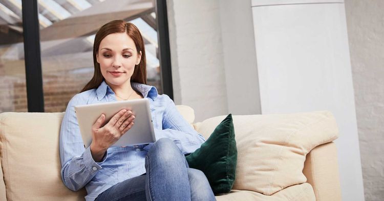Frau sitzt auf einem Sofa und schaut auf ihr Tablet