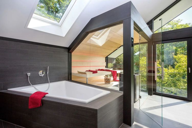 Wellnessbadezimmer mit großer Glasfront, Badewanne und verglaster Indoor-Sauna für den Blick ins Grüne