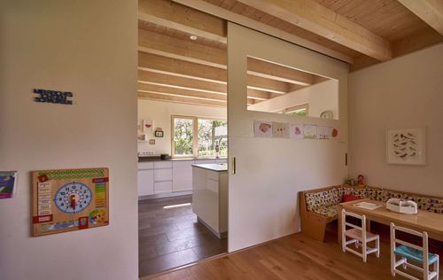 Die Kinderecke des modernen Holzhauses im Landhausstil mit Holzfassade aus Lärchenholzbohlen und Doppelcarport