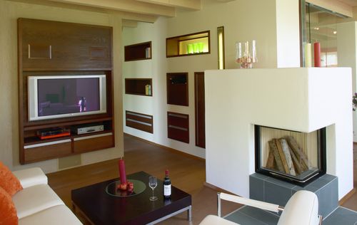Das Wohnzimmer des Holzhauses im Landhausstil mit geschickt eingesetzte Mischfassade aus mineralischem Außenputz und Lärchenholz und Schiebläden, die elektrisch verstellbar sind