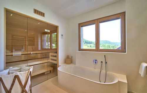 Das Badezimmer des modernen Holzhauses mit drei Gebäudetrakten, davon zwei mit mineralischem Außenputz und einer mit Holzverschindelung, alle mit Flachdach und im Bauhausstil mit Sauna