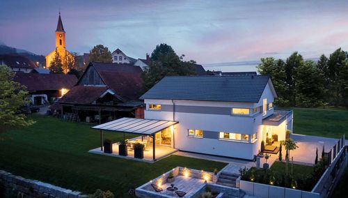 Modernes Fertighaus mit Satteldach und Terrasse mit Pergola bei Abendbeleuchtung