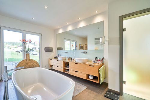 Das helle Bad mit freistehender Badewanne des modernen Bungalows aus Holz im Bauhausstil mit mineralischem Außenputz mit Pool