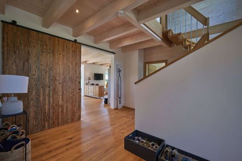 Die Diele des modernen Holzhauses im Landhausstil mit durchgängiger Lärchenholzfassade und Holz-Alu-Fenstern mit großer Schiebetür