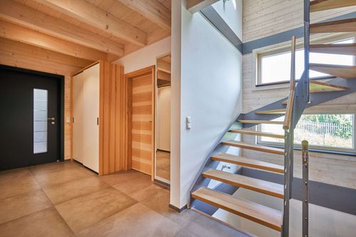 Die Diele mit Treppe des modernen Holzhauses im Landhausstil mit Holzfassade, Holz-Alu-Fenstern und großzügigen Balkonen