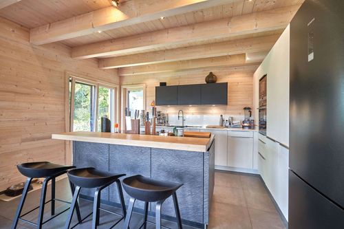 Die Küche des modernen Holzhauses im Landhausstil mit Holzfassade, Holz-Alu-Fenstern und großzügigen Balkonen