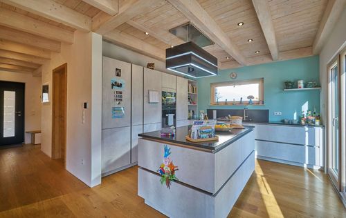 Die Küche des modernen Holzhauses im voralpenstil mit Mischfassade aus Lärchenholz und mineralischem Putz, Anbau mit Flachdach