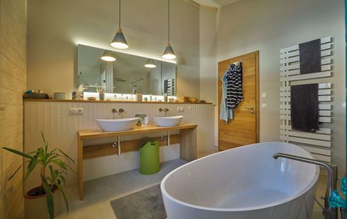 Das Badezimmer des modernen Holzhauses im voralpenstil mit Mischfassade aus Lärchenholz und mineralischem Putz, Anbau mit Flachdach mit freistehender Badewanne