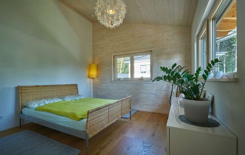 Das Schlafzimmer des modernen Holzhauses im voralpenstil mit Mischfassade aus Lärchenholz und mineralischem Putz, Anbau mit Flachdach