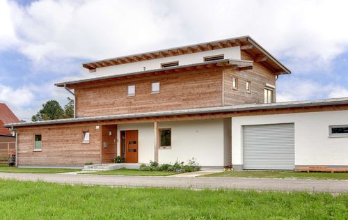 Der Eingang des modernen Holzhauses mit Pultdach und gemischter Fassade aus mineralischem Putz und Lärchenholz