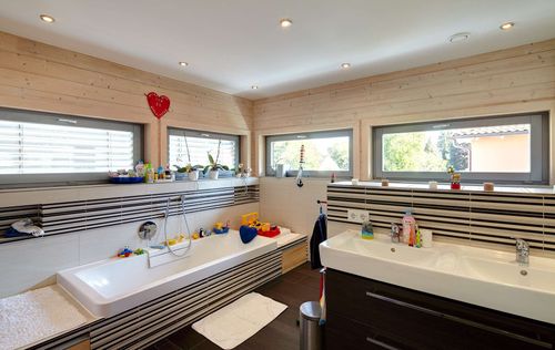 Das Badezimmer mit Badewanne und Doppelwaschbecken des Holzhauses im Landhausstil mit durchgängiger Holzfassade und großer Glasfront