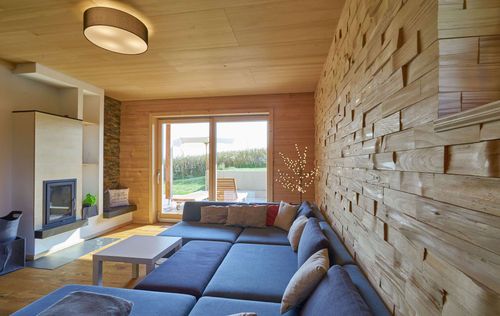 Das Wohnzimmer des modernen Holzhauses mit Holzverschindelung aus Tannenholz und geschützem Balkon- und Terrassenbereich