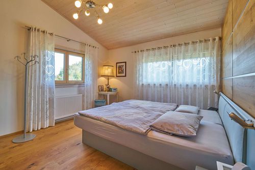 Das Schlafzimmer des modernen Holzhauses im Landhausstil mit flachem Satteldach und gemischter Fassade aus Lärchenholz und mineralischem Außenputz