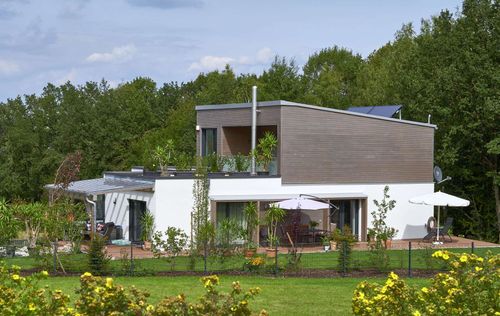 Modernes Holzhaus im Bauhausstil mit drei Gebäudetrakten, zwei davon mit mineralischem Außenputz und Flachdach, einer mit Holzfassade aus Fichtenholzbohlen und Pultdach