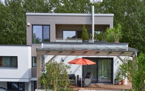 Die obere Terrasse des modernen Holzhauses im Bauhausstil mit drei Gebäudetrakten, zwei davon mit mineralischem Außenputz und Flachdach, einer mit Holzfassade aus Fichtenholzbohlen und Pultdach