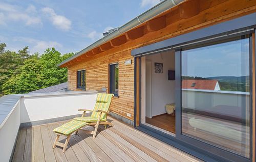 Der Balkon des modernen Holzhauses im Landhausstil mit Mischfassade aus Fichtenholz und mineralischem Außenputz