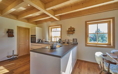 Die Küche des traditionellen Holzhauses mit durchgängiger Holzfassade, innen viel sichtbarem Holz und moderner Haustechnik